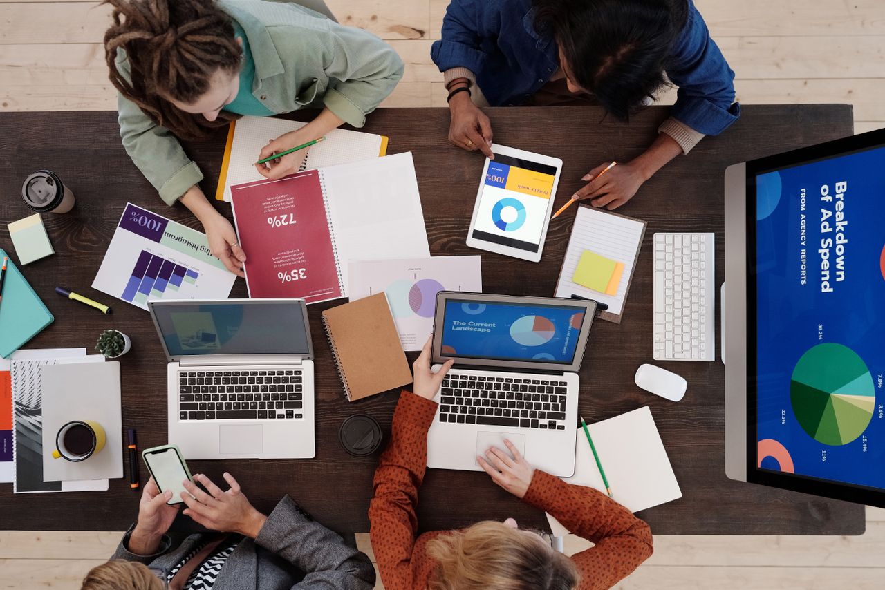 Une équipe diversifiée travaille ensemble sur des stratégies de marketing digital autour d’une table, avec des ordinateurs portables et des tablettes.